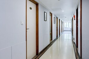 Un pasillo largo y estrecho con puertas a ambos lados, suelo de baldosas y un techo luminoso.