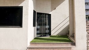 L’entrée d’un immeuble se compose d’une porte en verre, d’un escalier et d’une petite portion de gazon artificiel.