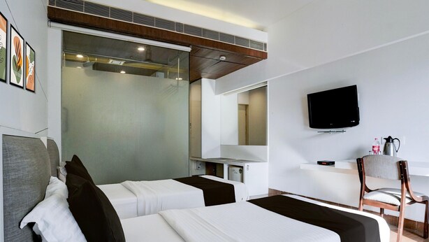 Une chambre d’hôtel avec deux lits, une télévision, un bureau avec une chaise et une fenêtre avec des stores.
