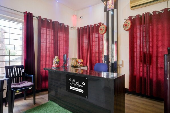 Uma mesa de recepção com um letreiro, uma cadeira e uma cadeira de escritório azul, além de cortinas vermelhas.