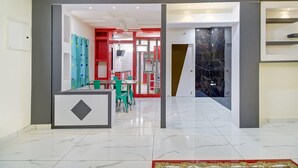 Un vestíbulo de hotel con piso de mármol, una mesa de recepción y una zona de juegos para niños con sillas y mesas verdes.