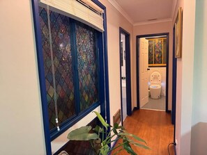 Ein Flur mit einem Buntglasfenster, einer zur Toilette führenden Tür und einer Pflanze.