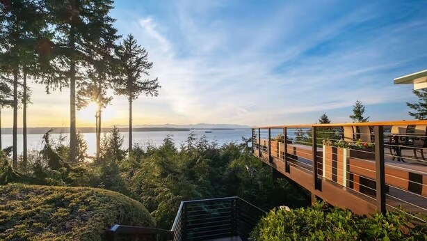 A modern outdoor staircase leading to a deck overlooking a body of water, surrounded by trees and vegetation. - Epic views, beautiful location, private & quiet (Burien)