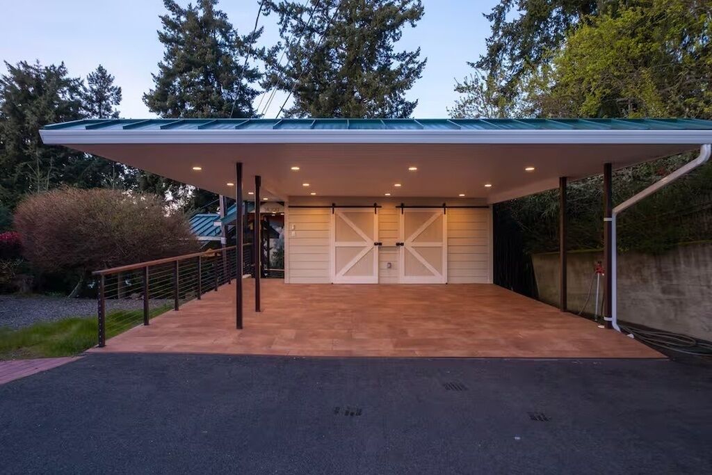 Een overdekte garage met een metalen dak, een houten terras en een toegangshek.