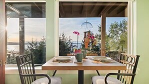 A dining table with chairs, a window with a view of trees and a building, and a hanging light fixture. - Epic views, beautiful location, private & quiet (Burien)