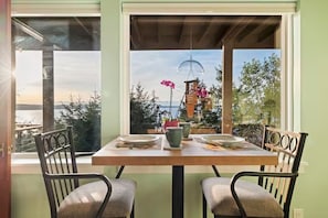 A dining table with chairs, a window with a view of trees and a building, and a hanging light fixture. - Epic views, beautiful location, private & quiet (Burien)
