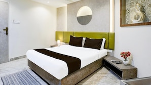 A modern hotel room with a large bed, a green headboard, a round wall decoration, a small table with a vase of flowers, and a ceiling fan. - Super Collection O Ghodbunder Road (Mumbai)
