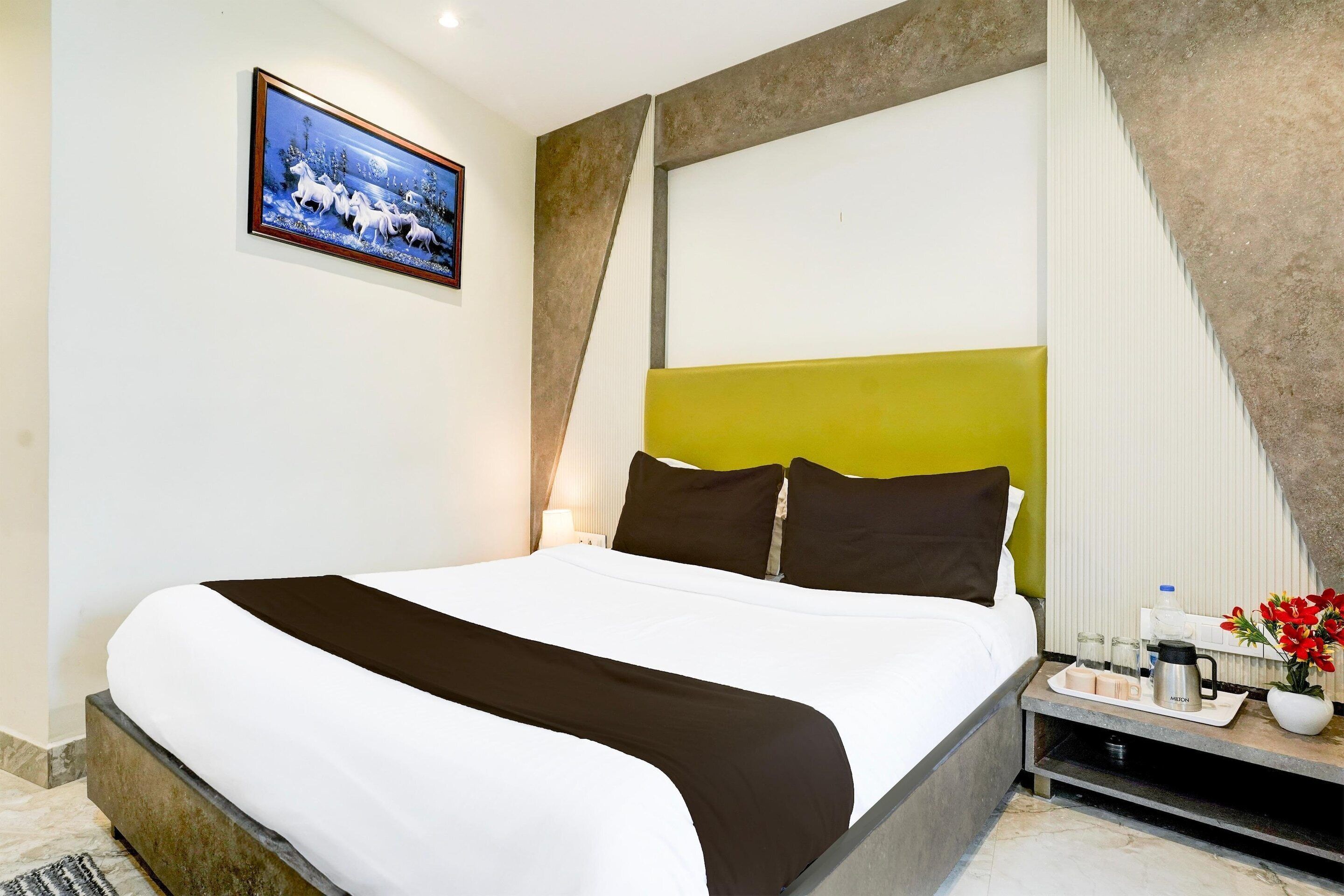 A neatly made bed with a white and brown bedspread, a bedside table with a tray of toiletries, and a framed picture on the wall.