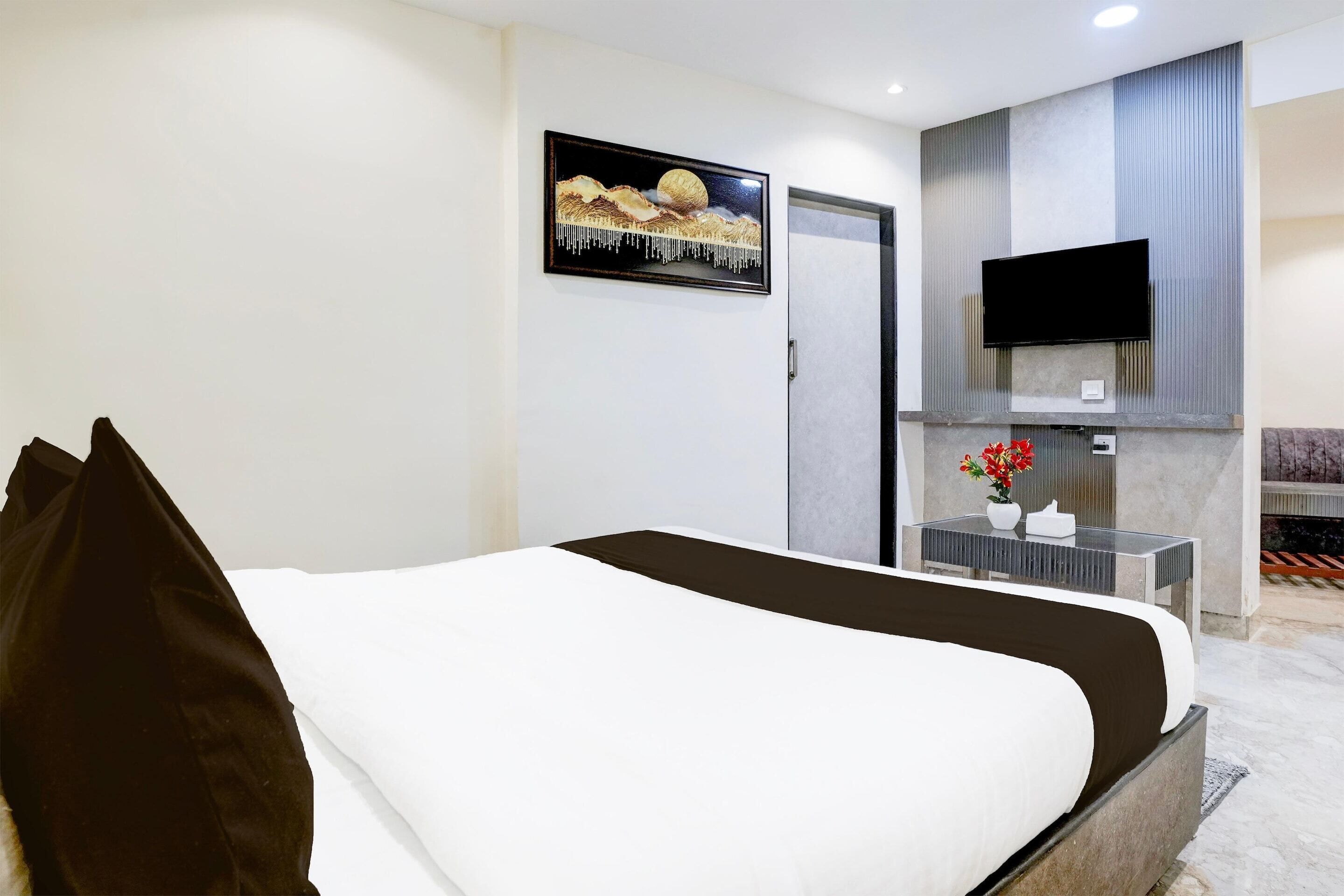 Habitación de hotel con cama, televisión de pantalla plana montada en la pared, una mesita con un jarrón de flores y chimenea.