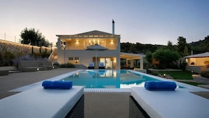Ein zweistöckiges Haus mit Swimmingpool, Sitzgelegenheit im Freien und einem gut beleuchteten Patio.