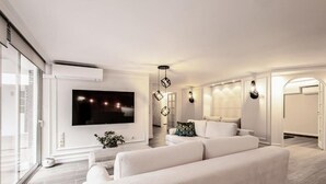 A modern living room with a flat-screen TV, a sofa, and a decorative light fixture. - MZ Kolonaki Hills (Athina)