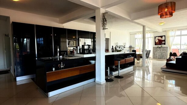 A spacious kitchen with a central island, a dining area with chairs, and a large window providing natural light. - Penthouse 3 min walk from Flic en Flac beach (Flic en Flac)