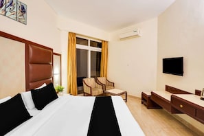 A hotel room with a bed, a desk, a chair, a TV, and a window with curtains.
