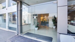 Un edificio moderno con amplios ventanales de vidrio, entrada de metal y plantas en macetas en el interior.