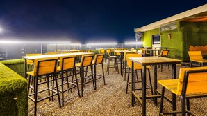 Un espacio al aire libre con mesas y sillas, una pared verde y vistas de la ciudad de noche.