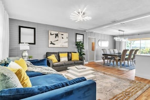 Ein modernes Wohnzimmer mit einem blauen Sofa, einem Essbereich mit Tisch und Stühlen sowie einer Küche im Hintergrund.