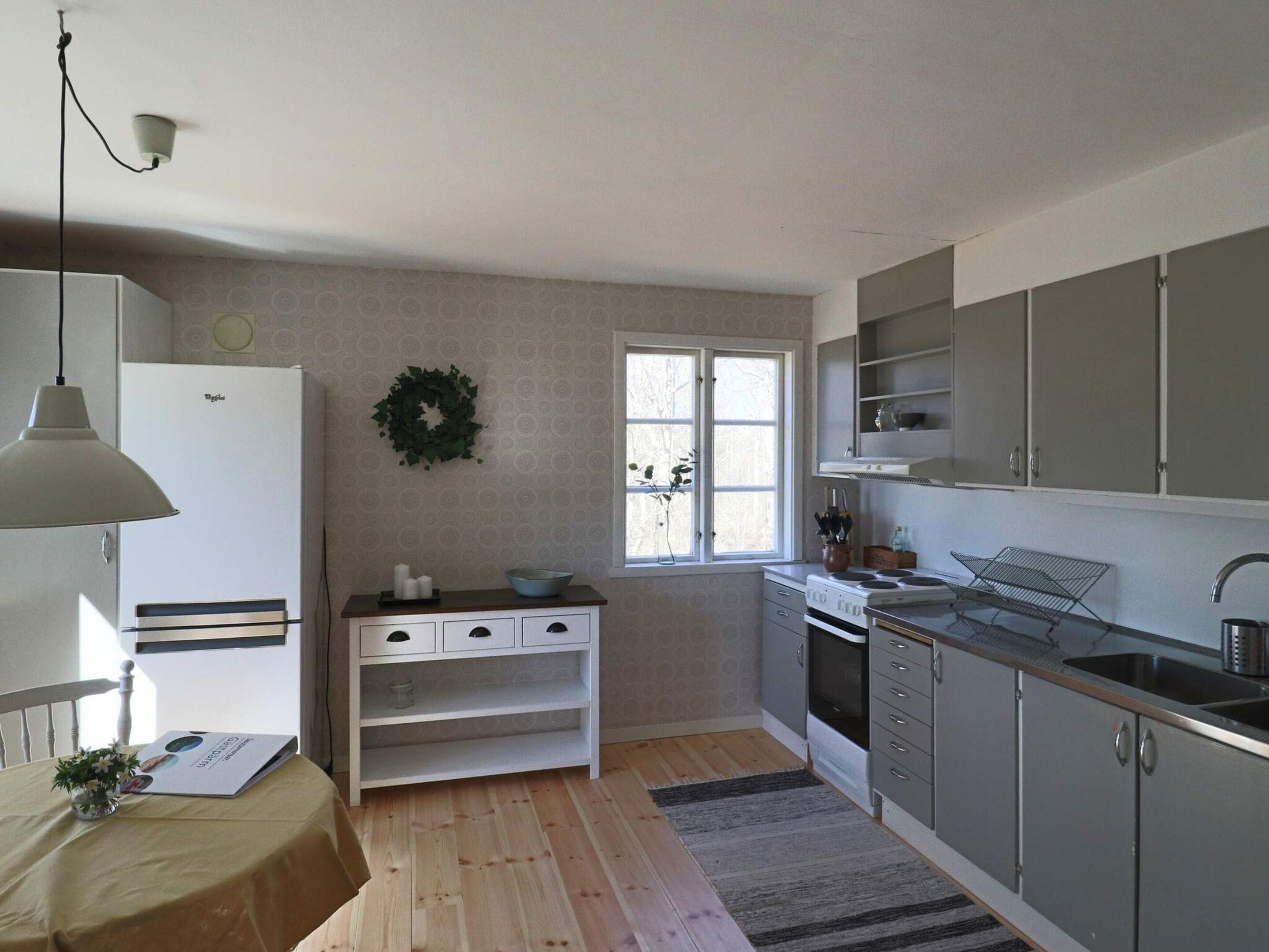 Cocina compacta con refrigerador, lavamanos y estufa. Se ve una ventana con vista a árboles.
