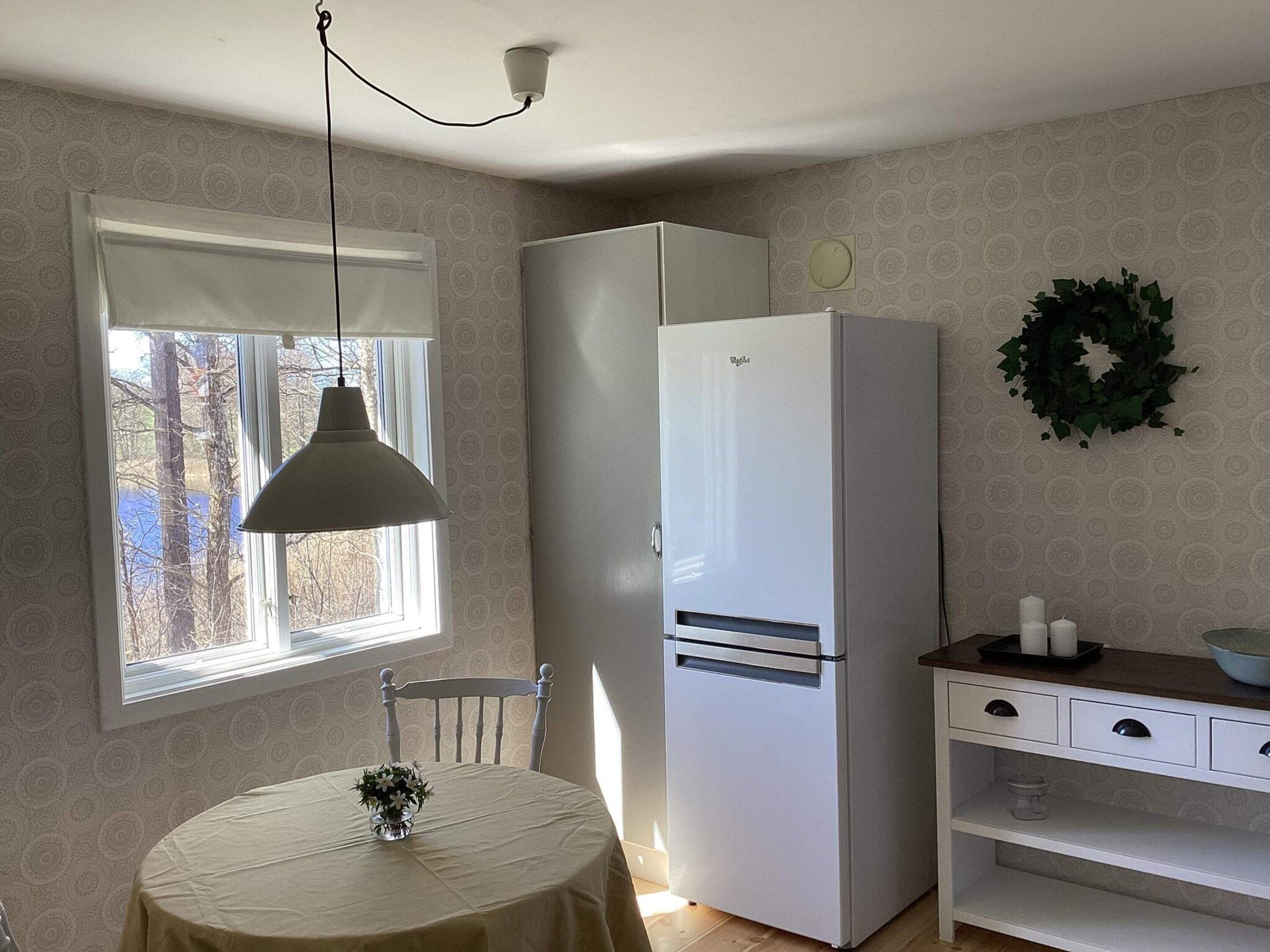 Una cocina con un refrigerador blanco, una mesa de comedor con un florero y una ventana que da a las árboles.