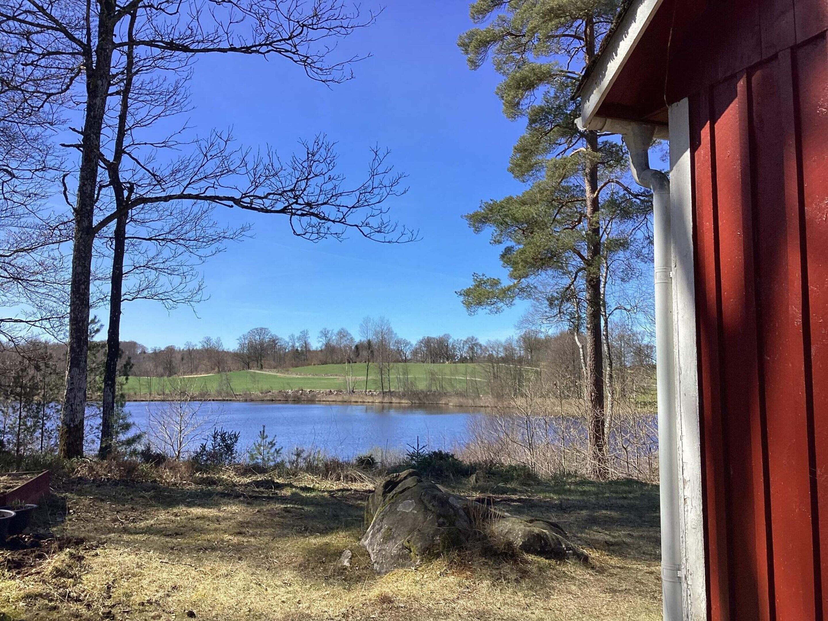 Blick auf einen See mit einem roten Gebäude, Bäumen und einer grünen Wiese.
