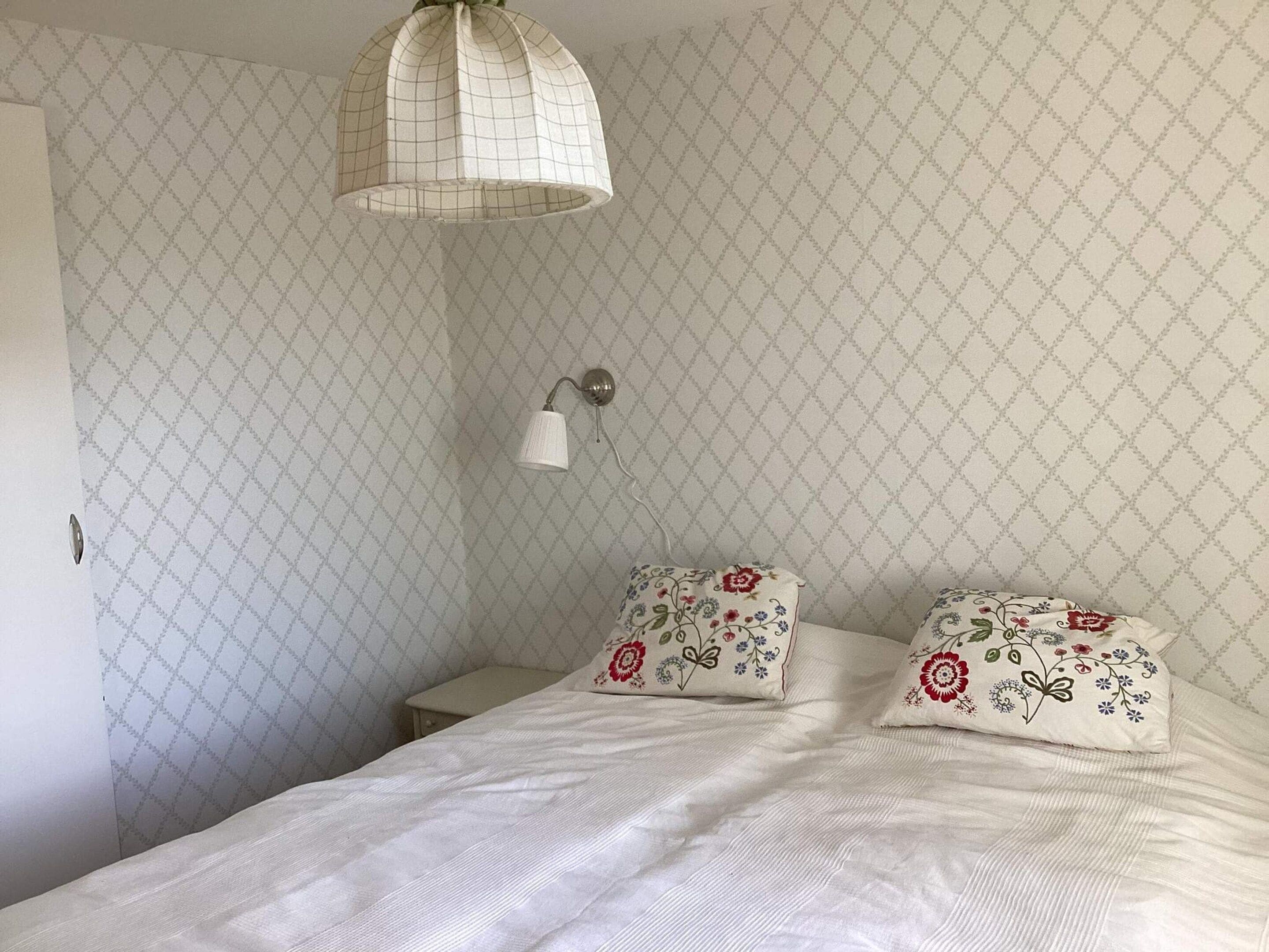 Un dormitorio con cama, dos almohadas, una mesita de noche, una lámpara de pared y una lámpara colgante.