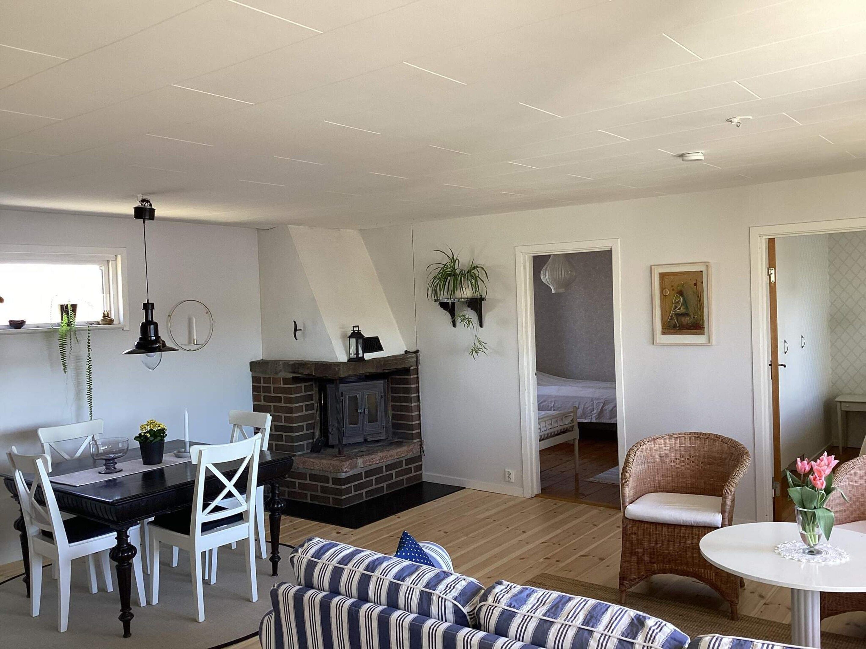 A living room with a fireplace, dining table, white chairs, a striped sofa, and a wicker chair.