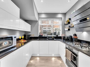 A modern kitchen with white cabinets, a black countertop, a built-in oven, and a window with blinds.