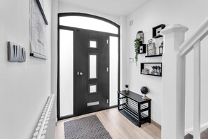A hallway with a black door, a radiator, a patterned rug, a small table with a globe, and shelves with decorative items.