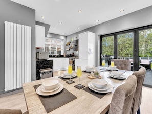 A modern kitchen with a dining area, large windows, and a view of the outdoors.