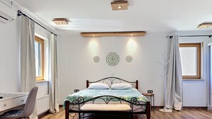 Um quarto com piso de madeira, uma cama com colcha estampada, uma escrivaninha com cadeira e uma janela com cortinas.