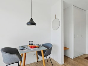 Ein moderner Essbereich mit Tisch, zwei Stühlen, einer Pendelleuchte, einem Wandspiegel und einer Tür.