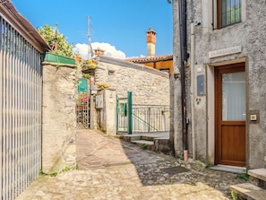Eine schmale Kopfsteinpflasterstraße führt zu einem Steinhaus mit einer Holztür und einem Schild, auf dem 'LA TERZA CASA' steht.