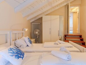 A bedroom with two beds, a radiator, a fan, and a staircase leading to an upper level. - La Terza Casa by Interhome (Tremezzina)
