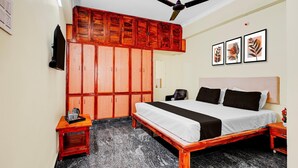 A bedroom with a bed, wooden wardrobe, ceiling fan, artwork, and a small table with a kettle. - Super Hotel O Tirupati Chennai (Tirupati)