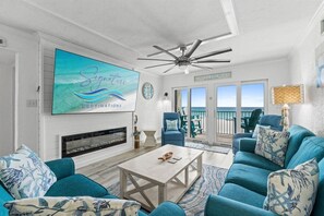 A living room with a television, a ceiling fan, a fireplace, and a view of the ocean through the sliding glass doors. - 2BR Pet Friendly Beach View Pool Sleeps 7 Condo! (Panama City Beach)