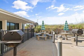 Un patio al aire libre con una parrilla, mesas y sombrillas.