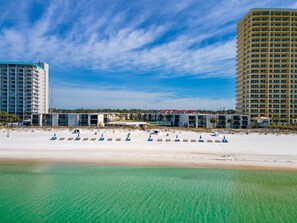 Un hôtel situé en bord de mer, composé de plusieurs bâtiments, avec une plage de sable fin et un ciel d’un bleu limpide.