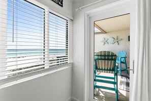 A room with a view of the ocean through blinds, a door leading to an outdoor area with chairs, and a wall decoration. - 2BR Pet Friendly Beach View Pool Sleeps 7 Condo! (Panama City Beach)
