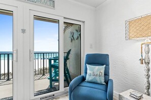 Ein Zimmer mit blauem Sessel, einer Glastür, die auf einen Balkon mit Meerblick führt, und einem Schild mit der Aufschrift 'Vorsicht, einsteigen'.