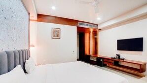 A modern hotel room with a large bed, a flat-screen TV mounted on the wall, a wooden console table, and a ceiling fan. - Palette Patel Nagar (Bhopal)