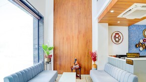 A reception area with a wooden panel wall, a reception desk, two sofas, a small table, and decorative items. - Palette Patel Nagar (Bhopal)