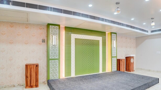 A hotel lobby with a patterned wall, a green accent wall, and a grey carpeted area. - Palette Patel Nagar (Bhopal)