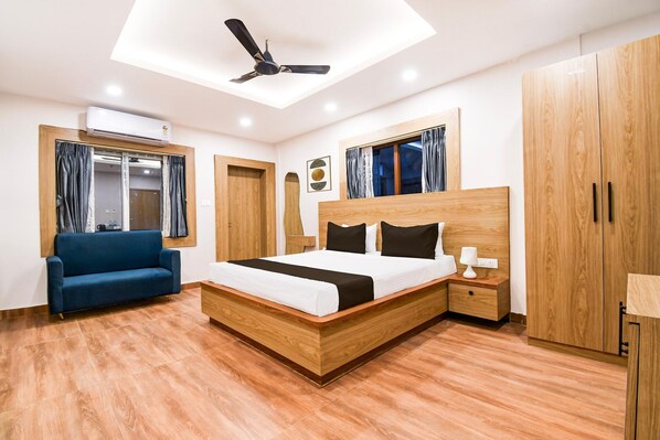 A modern bedroom with a wooden bed, a blue sofa, and a ceiling fan. - Super Deluxe Roompalette Jagannath Puri (Puri)