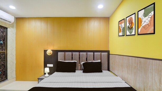 A modern bedroom with a large bed, wooden panel walls, a nightstand with a lamp, and three framed artworks on the wall. - Deluxehotel Virat Inn (Gorakhpur)