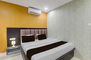 Una habitación de hotel con cama, mesita de noche, lámpara y un equipo de aire acondicionado.