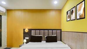 A hotel room with a bed, a nightstand, a wall-mounted lamp, and three framed artworks. - Deluxehotel Virat Inn (Gorakhpur)