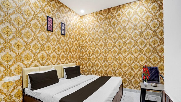 A hotel room with a patterned wallpaper, a bed with a headboard, a bedside table with a vase of flowers, and a small table with a decorative item. - Hotel O by OYO Silver Arc Mall Ludhiana (Ludhiana)