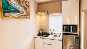 A compact kitchen with a gas stove, a microwave, and a stainless steel refrigerator. - Happy Lodge Shortlets & Suites (Lekki)