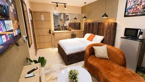 A compact hotel room with a bed, a sofa, a small kitchen area, and a television. - Happy Lodge Shortlets & Suites (Lekki)