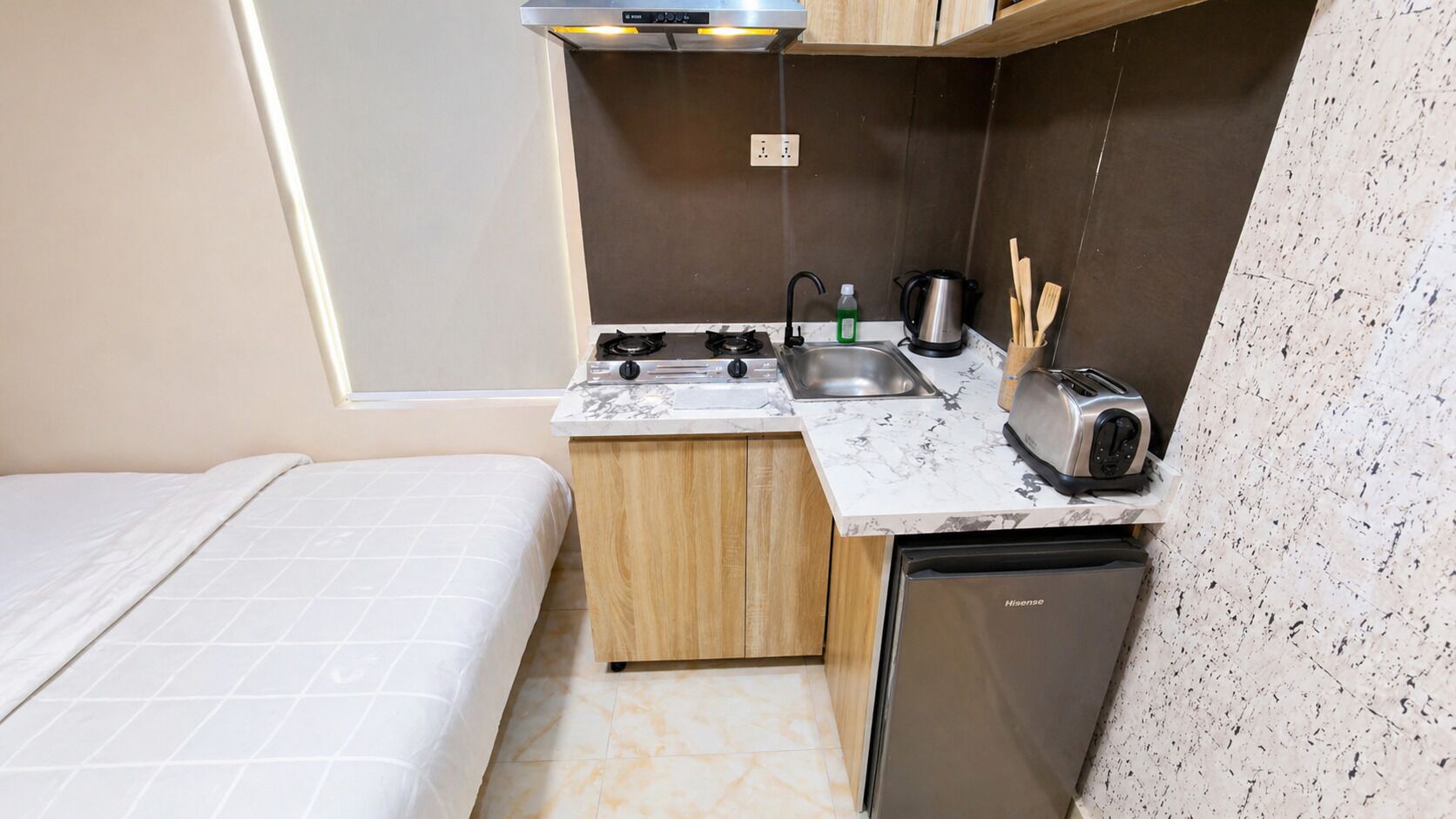 A compact kitchenette with a stove, sink, and toaster, a small wooden cabinet, and a compact dishwasher.