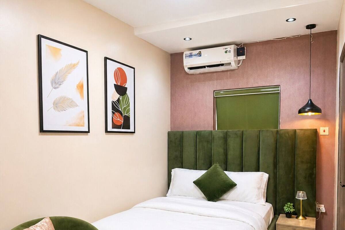 Quarto com cama, uma poltrona verde, mesa de cabeceira com abajur e ar condicionado.